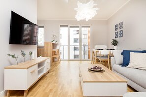 A modern living room with a flat-screen TV, wooden furniture, a dining area, and a large window with a city view. - Business Mokotow Park 214 Apartment (Warsaw)