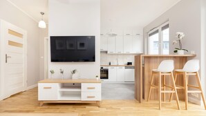 A modern kitchen with white cabinets, a wooden countertop, and a TV mounted above the counter. There are two white bar stools and a small potted plant on the counter. - Business Mokotow Park 214 Apartment (Warsaw)