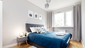 A modern bedroom with a large bed, a bedside table with a lamp, and a window with curtains. - Business Mokotow Park 214 Apartment (Warsaw)