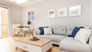 A modern living room with a grey sofa, a wooden coffee table, and a dining area with a white table and chairs. - Business Mokotow Park 214 Apartment (Warsaw)