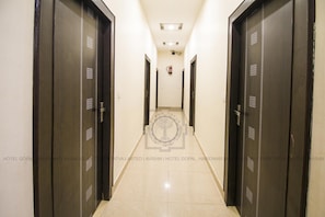 A hotel corridor with dark wooden doors, a tiled floor, and a fire extinguisher on the wall. - Hotel Gopal (Haridwar)