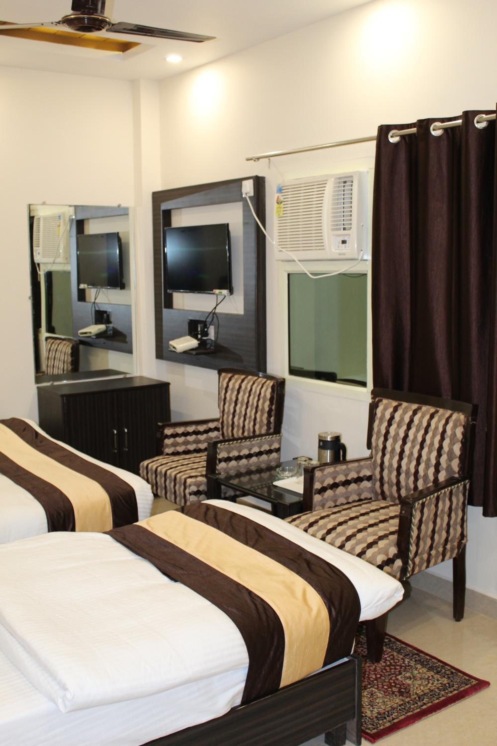 A hotel room with two beds, a television, a desk with a coffee maker, and a patterned armchair.