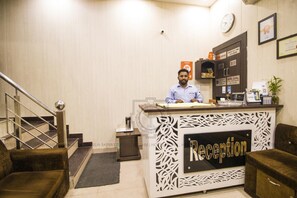 A reception desk with a sign that reads 'Reception,' a clock on the wall, and a staircase with a metal handrail. - Hotel Gopal (Haridwar)