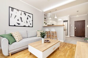 A modern living room with a sofa, coffee table, and artwork. There is a kitchen area with a counter and stools. - Business Mokotow Park 215 Apartment (Warsaw)