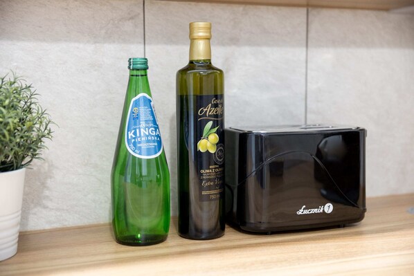 A bottle of Kinga beer, a bottle of olive oil, and a black Lucznik device on a wooden surface. - Business Mokotow Park 215 Apartment (Warsaw)