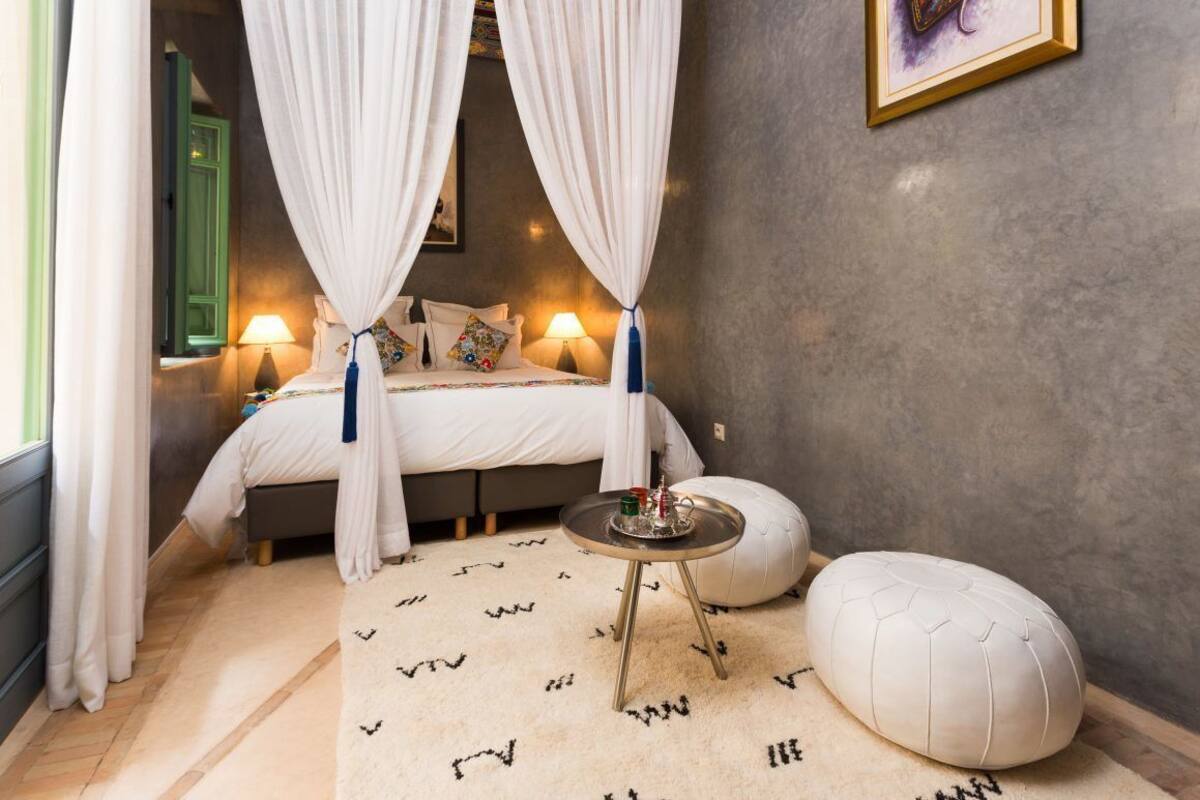 A bedroom with a bed, bedside lamps, a bedside table, a hanging light, a window with curtains, and a wall-mounted picture.