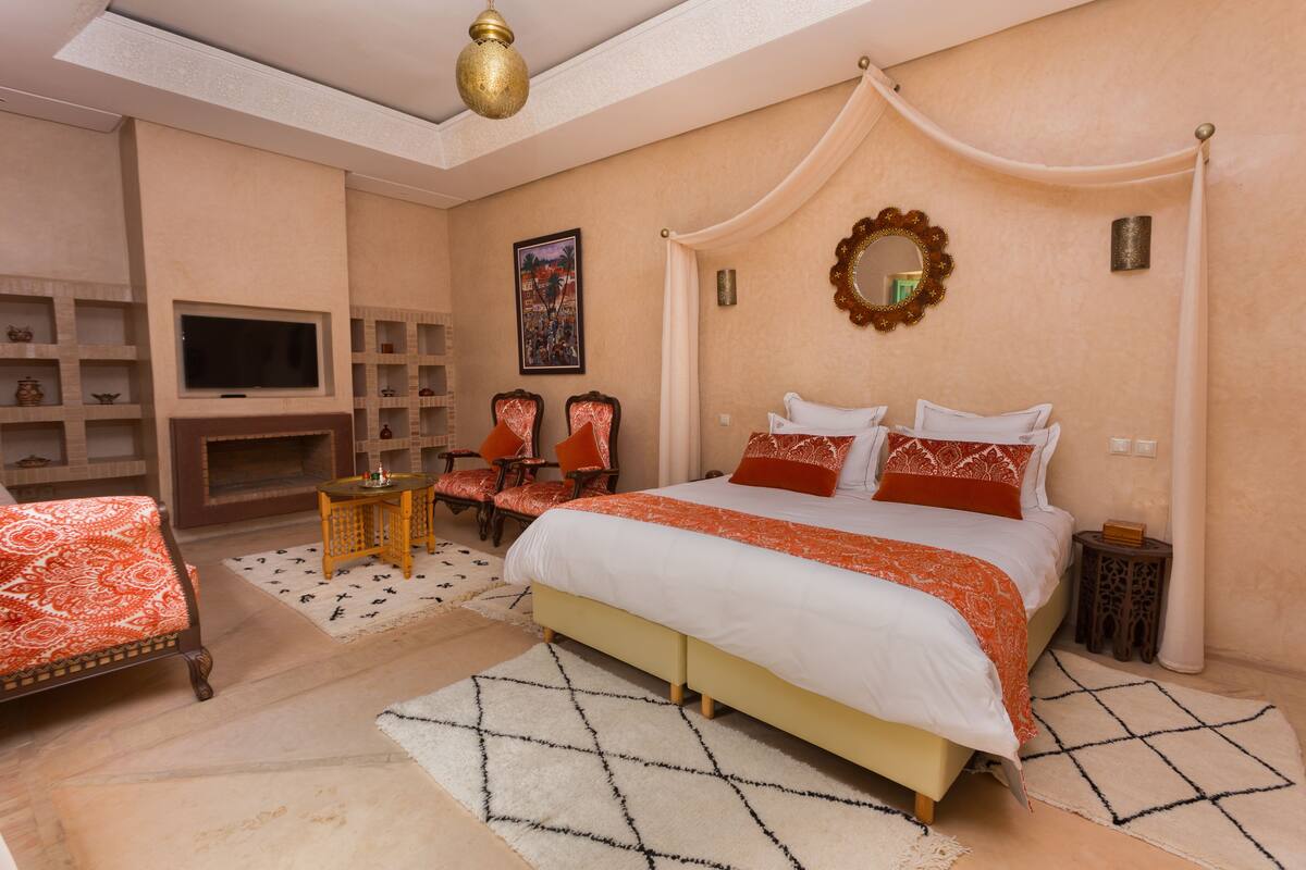 A bedroom with a large bed, a TV, a fireplace, and a seating area with chairs.