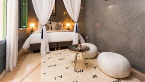A bedroom with a bed, bedside lamps, a bedside table, a hanging light, a window with curtains, and a wall-mounted picture. - Riad Azrur (Marrakech)