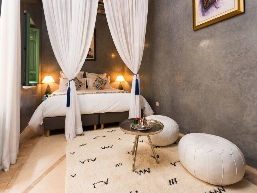 Une chambre à coucher comprenant un lit, des lampes de chevet, une table de chevet, une suspension, une fenêtre avec des rideaux et un tableau accroché au mur.