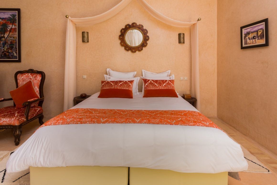 Una cama con dosel, dos almohadas, una mesita de noche y una silla con cojín.