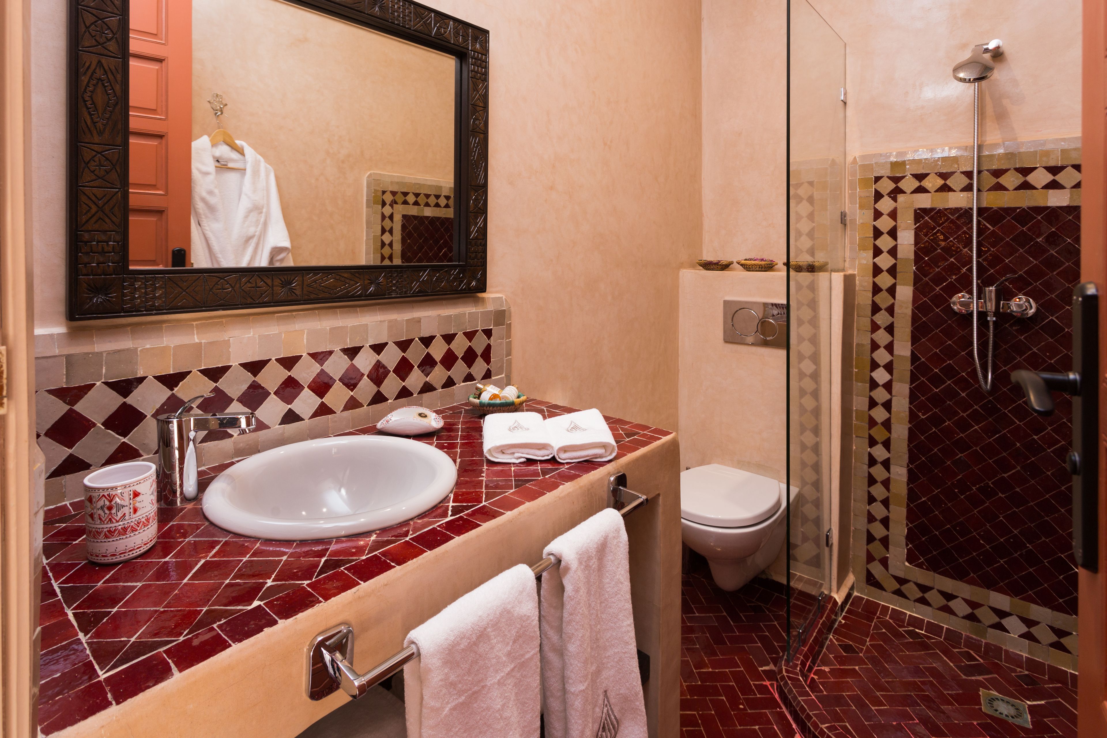 Une salle de bain avec un meuble-lavabo aux carreaux rouges, un lavabo blanc, un miroir, des toilettes et une douche à parois de verre.