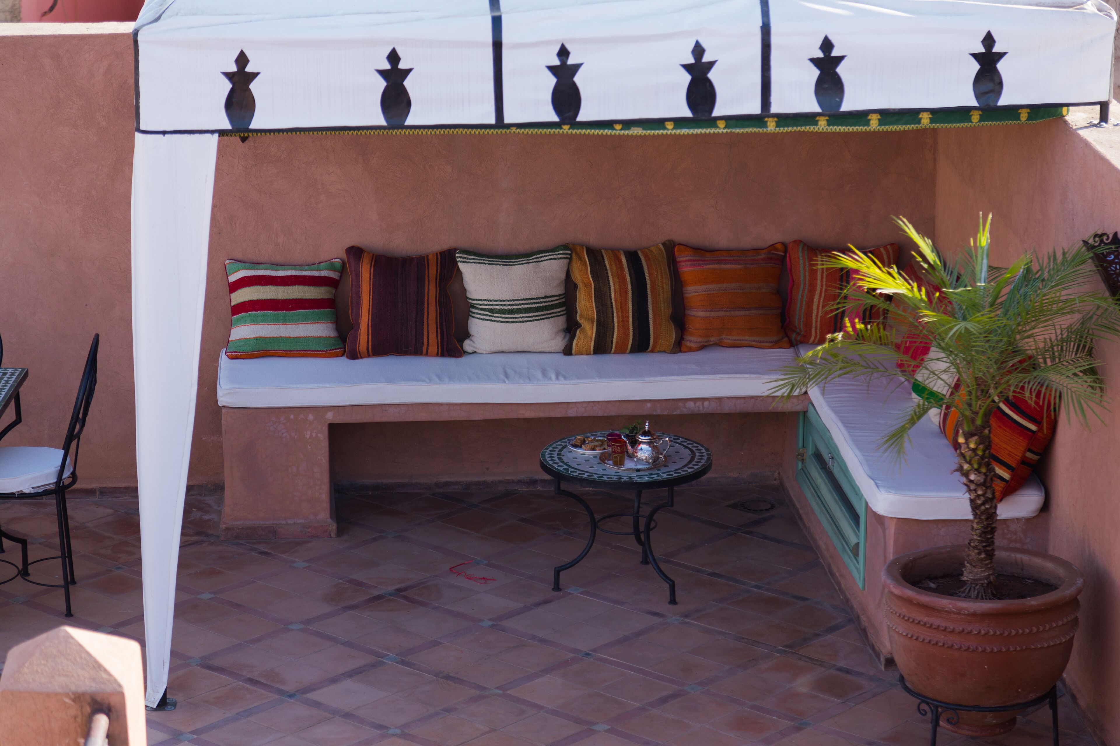 Eine Terrasse mit Sitzgelegenheit mit Kissen, einem kleinen Tisch und einem Blumentopf.