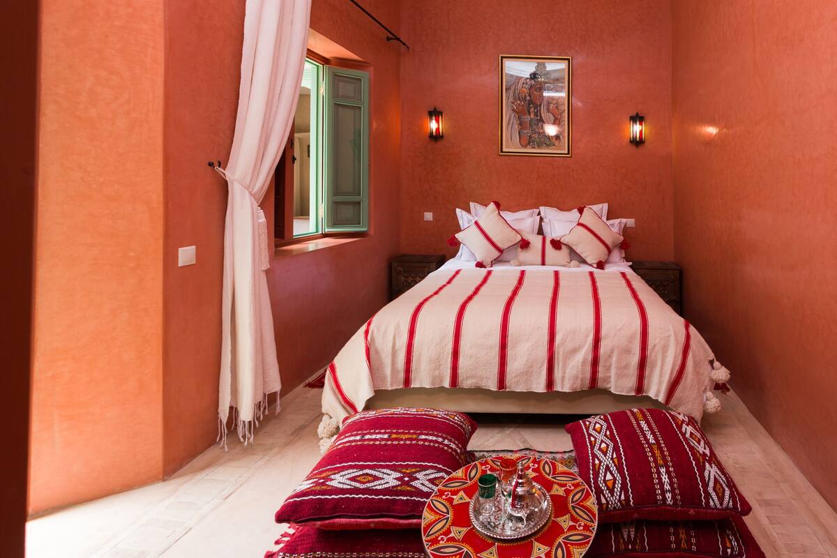 A bedroom with a bed, pillows, a wall-mounted light, and a window with curtains.