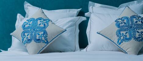 A bed with white bedding and two pillows with blue embroidery.