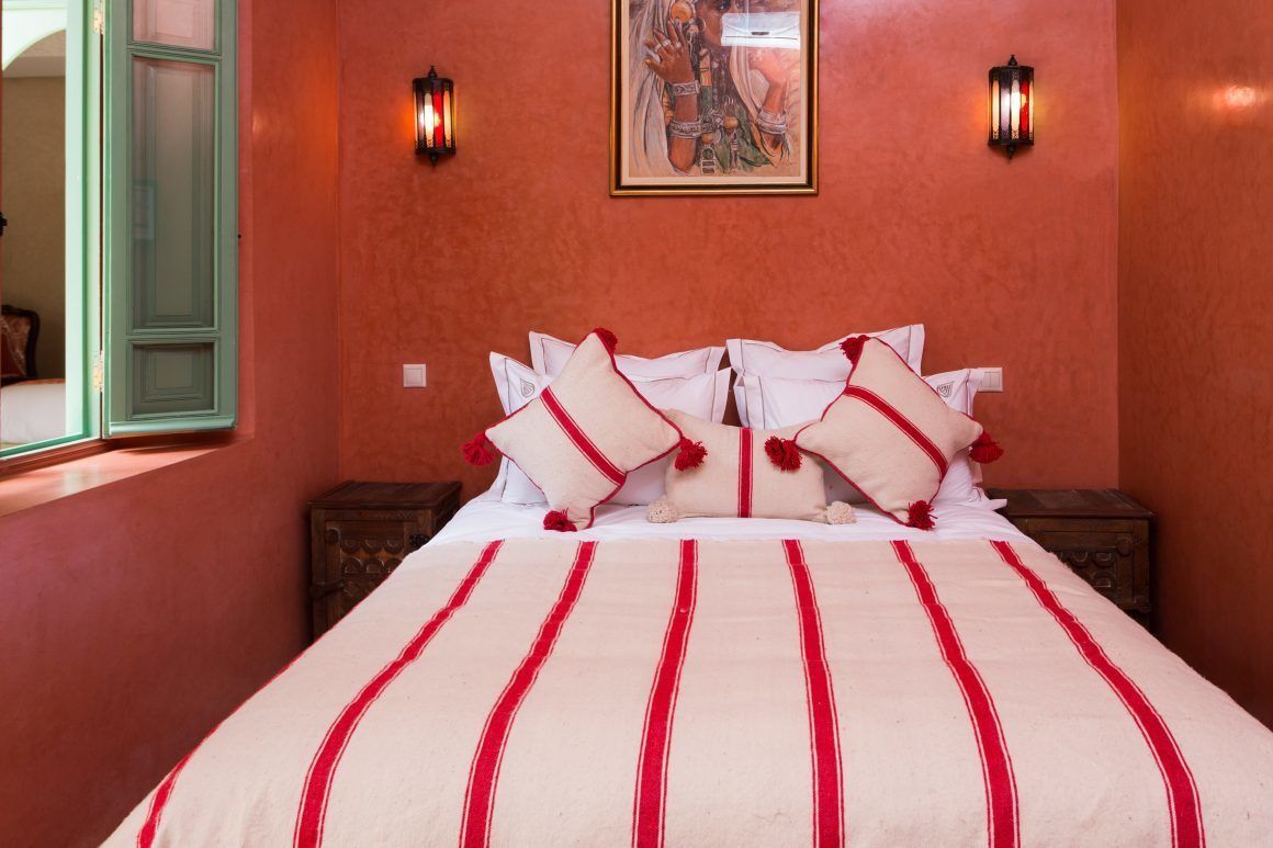 A hotel room with a bed, pillows, a wall-mounted painting, and two wall sconces.