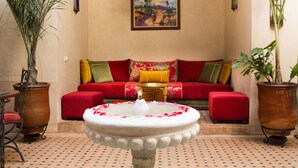 A cozy living room with a red sofa, a white fountain, and two potted plants. - Riad Azrur (Marrakech)