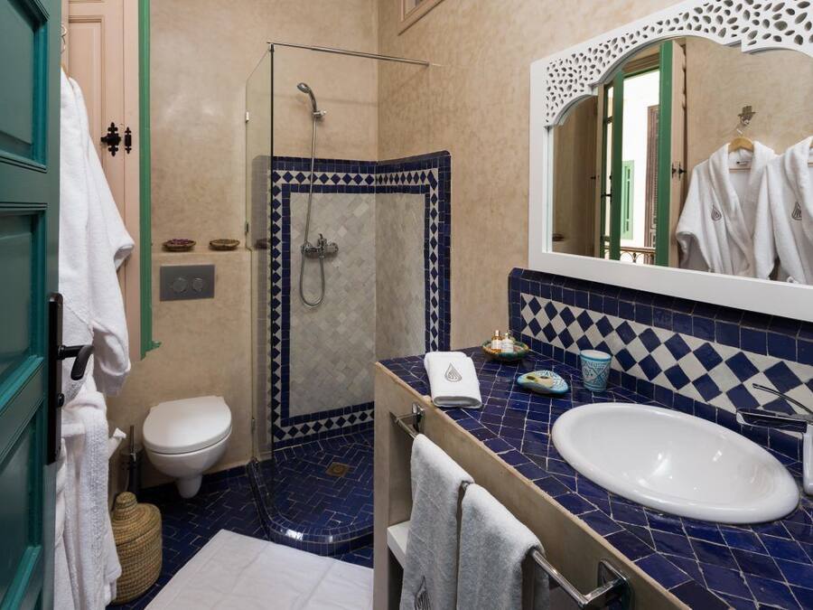 Une salle de bain équipée d’une douche, de toilettes et d’un lavabo, et dont le carrelage présente un motif bleu et blanc.