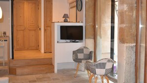 Une pièce avec des portes en bois, un téléviseur, deux fauteuils à carreaux et une fenêtre.