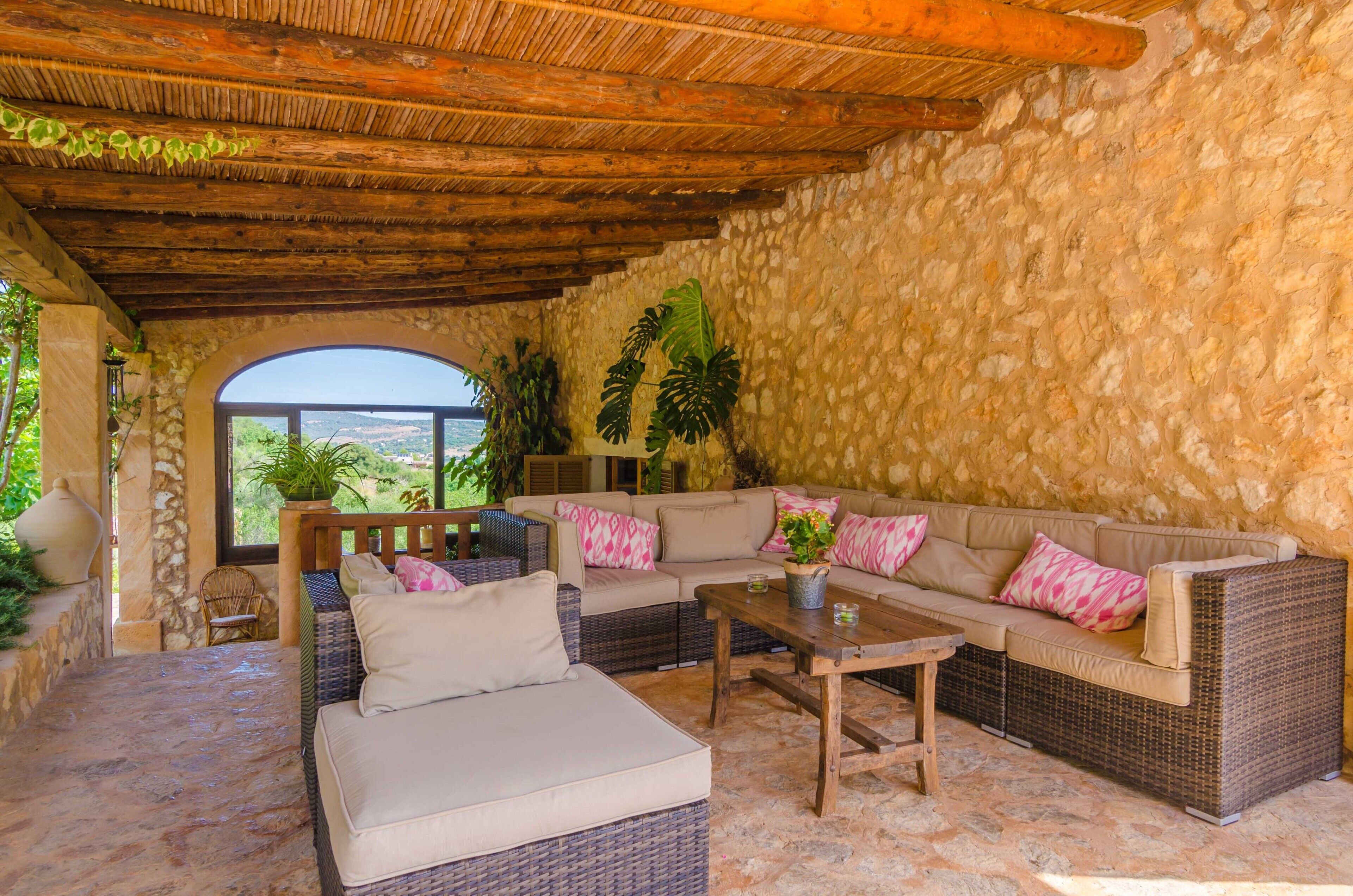 A cozy outdoor seating area with wicker furniture, a stone wall, and a view of the landscape.