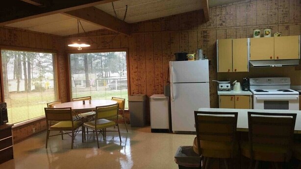 A compact kitchen with wooden walls, a dining table with chairs, a refrigerator, a stove, and a sink. - Beautiful Cabin Near Turtle Beach Lodge-ToledoBend Lake-Fishing (Many)