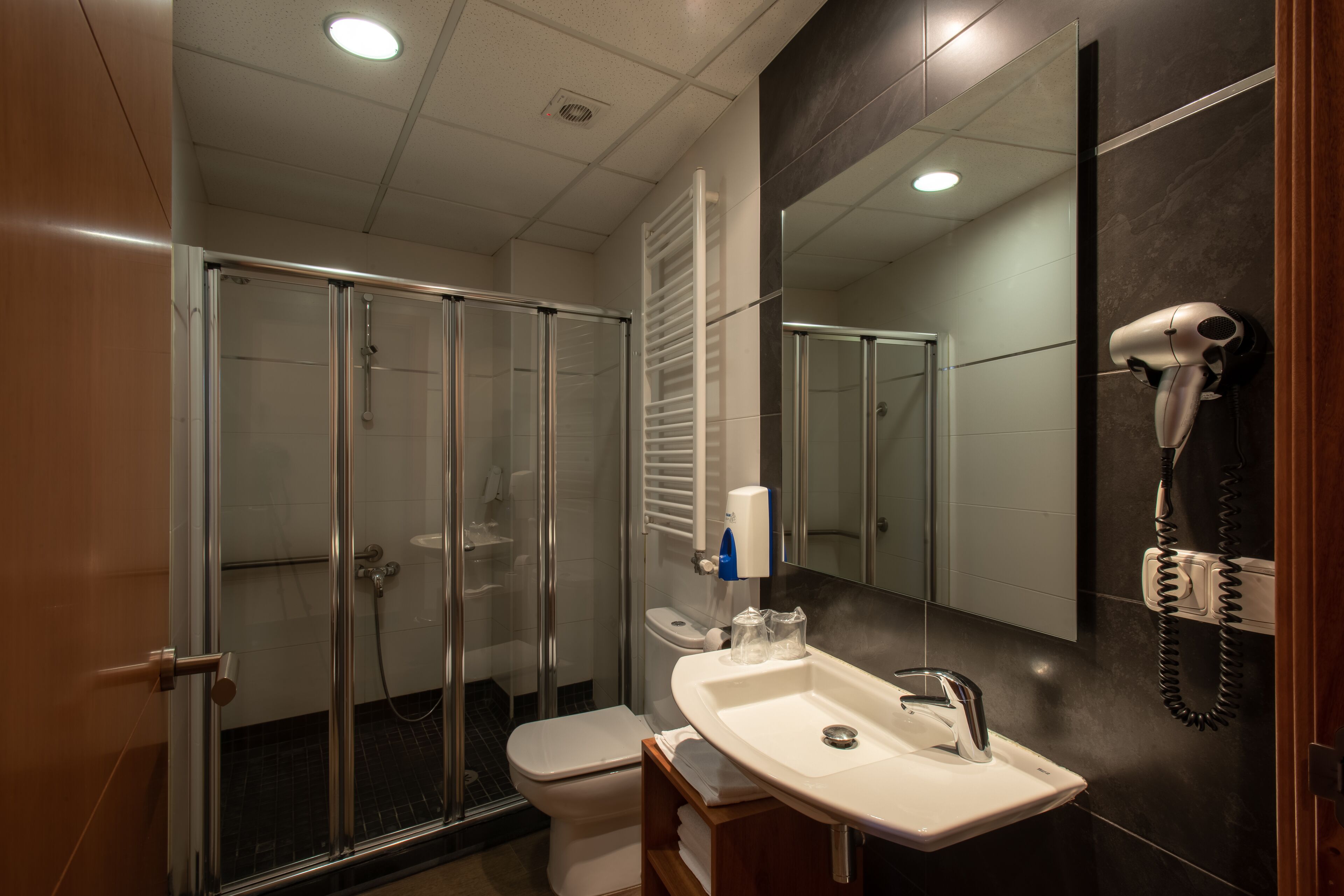 Ein modernes Badezimmer mit Duschkabine aus Glas, einem weißen Waschbecken mit Spiegel und einem an der Wand befestigten Föhn.