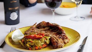 Een eettafel met een steak, groenten, een fles wijn en twee wijnglazen.
