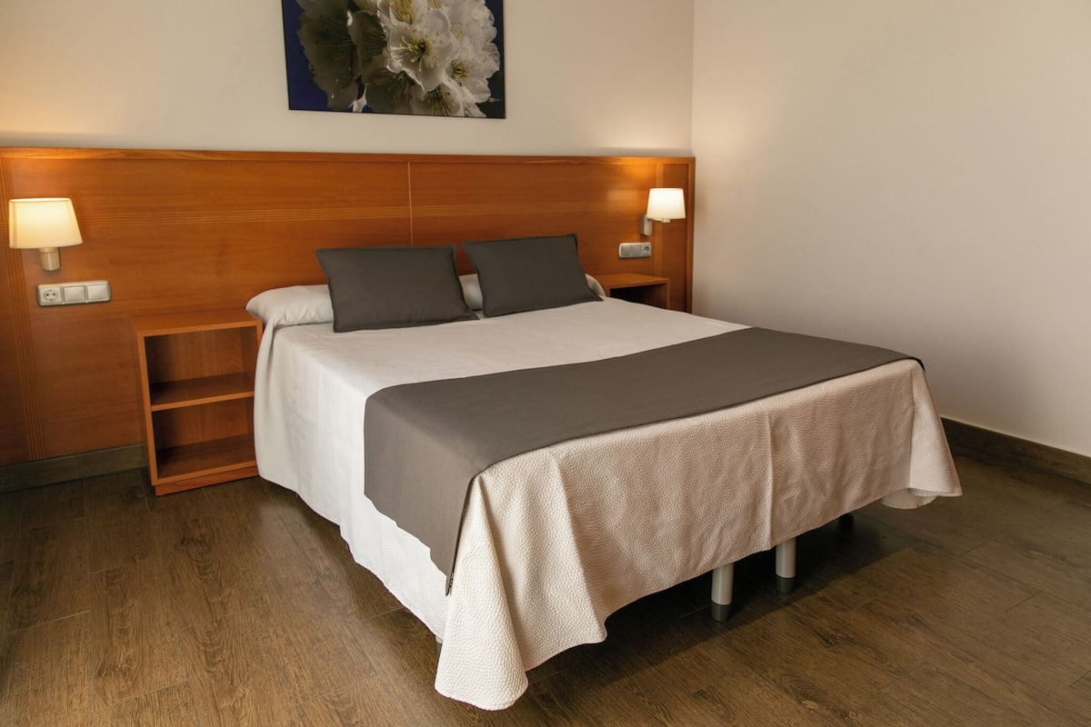 A neatly made bed with a wooden headboard, two bedside lamps, and a floral artwork above.