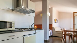Una cocina moderna con microondas integrado, estufa y campana extractora. Hay una zona de comedor con mesa y sillas, y un sofá al fondo.