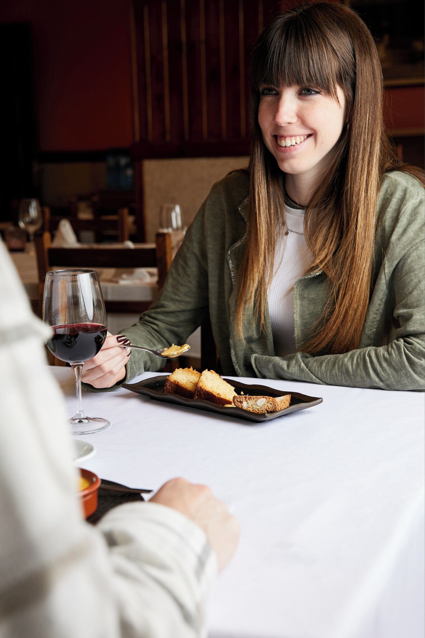 Una persona sentada a una mesa con un plato de comida y una copa de vino tinto.