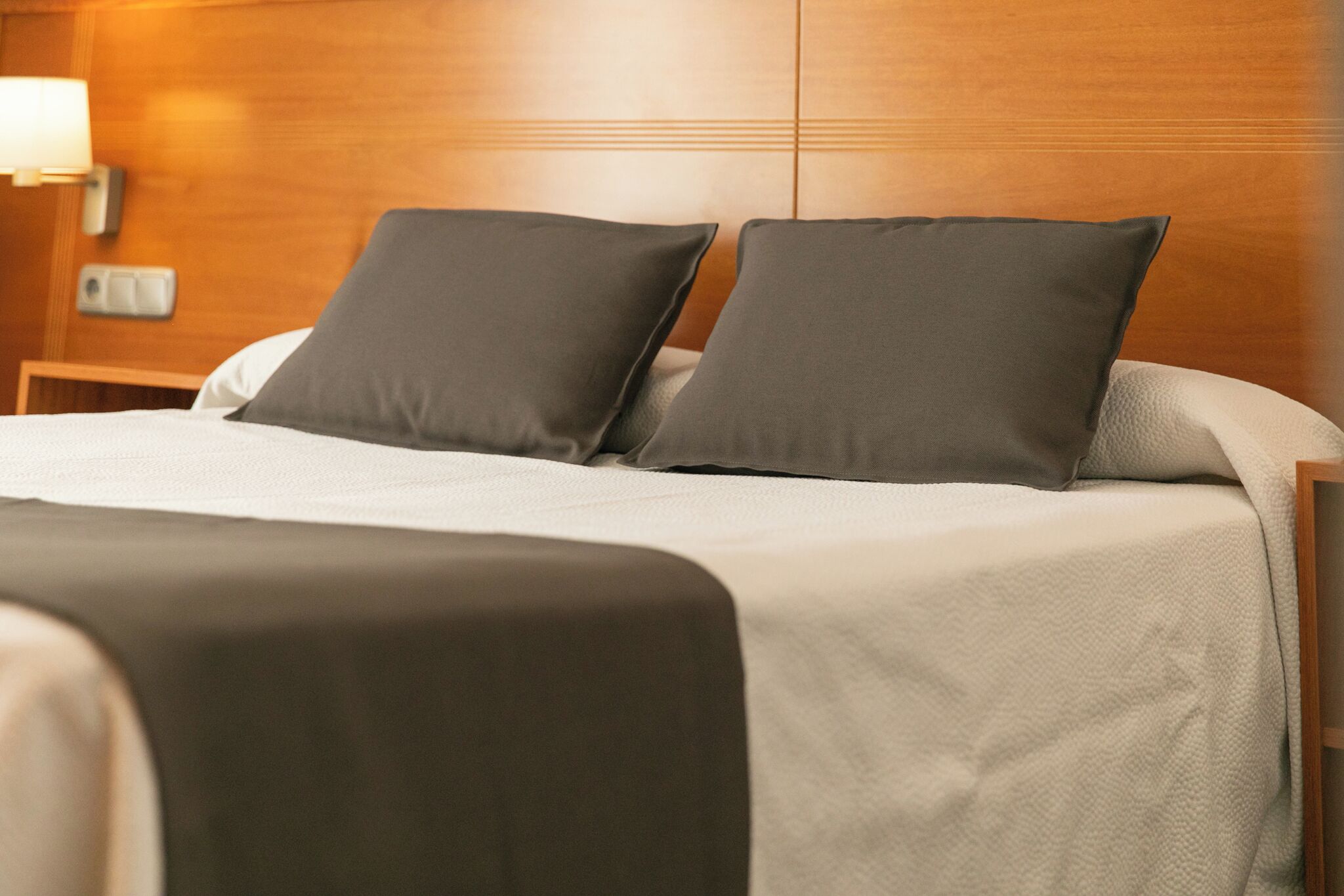 A neatly made bed with two pillows, a bedside lamp, and a wooden headboard.