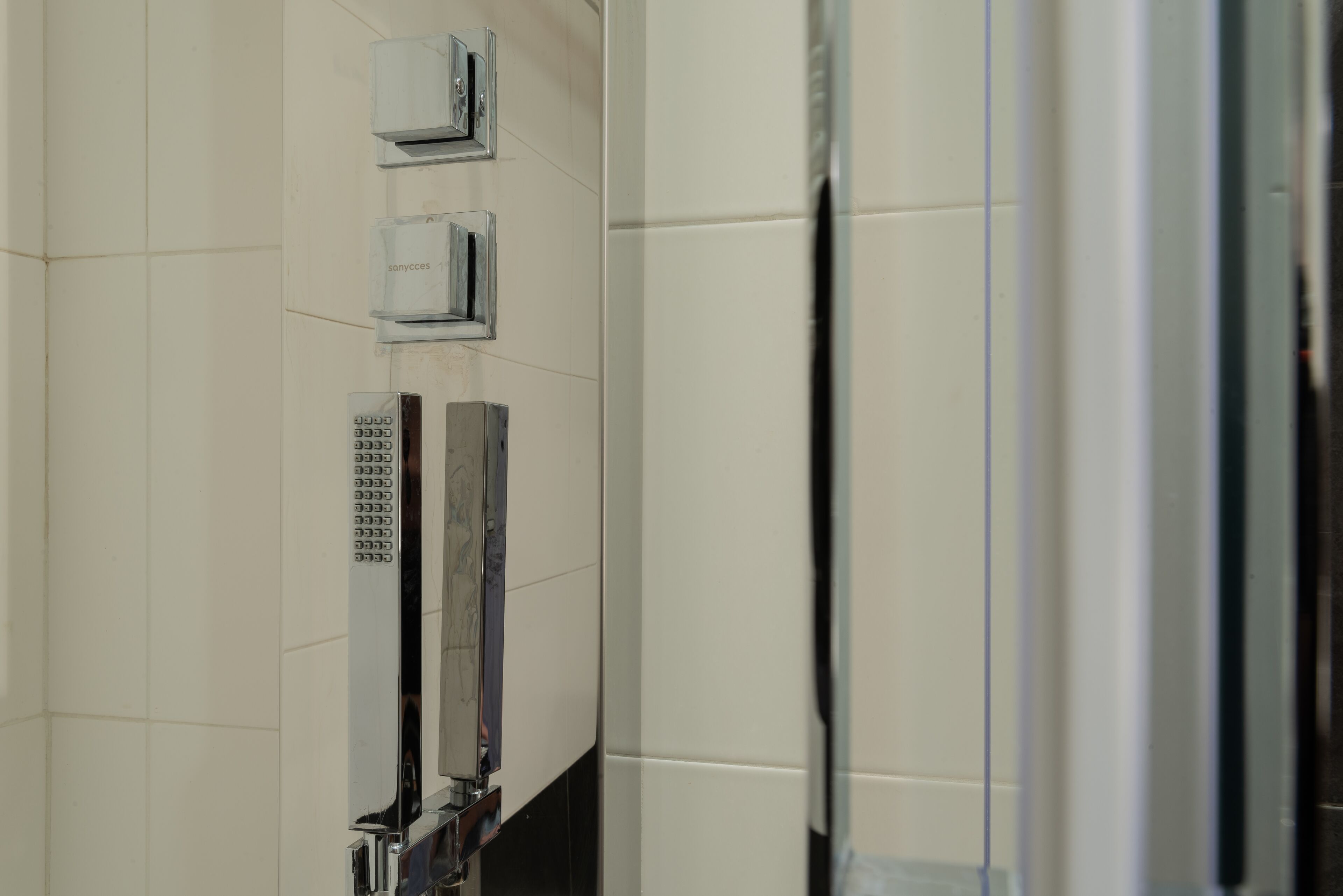 A bathroom with a tiled wall, a mirror, and a shower area.