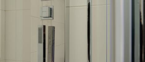A bathroom with a tiled wall, a mirror, and a shower area.