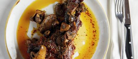 A plate of meat with sauce and a glass of red wine on a white table.