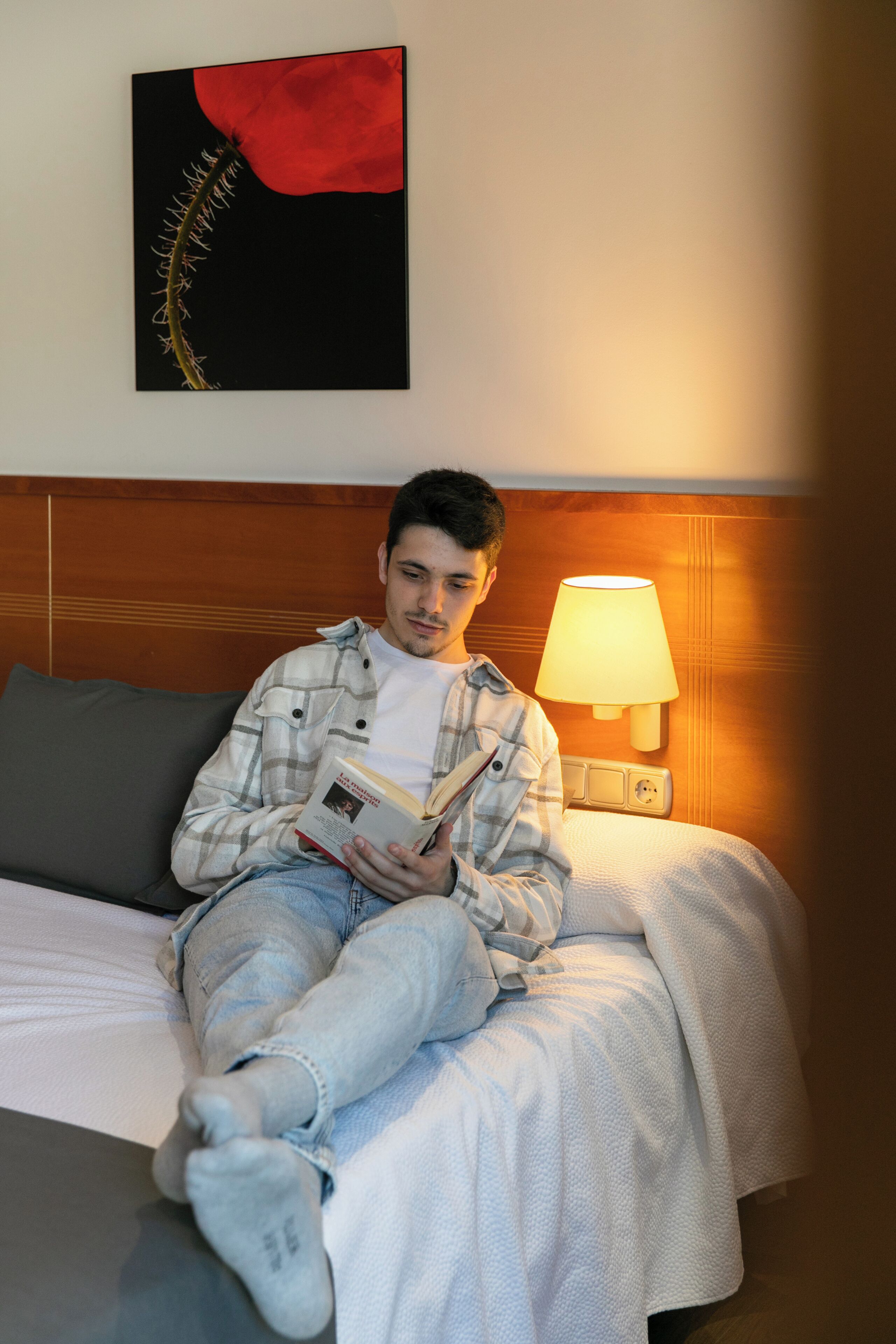 A person sitting on a bed in a hotel room, reading a book.