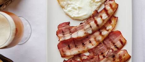 A breakfast plate with eggs and bacon, a fork, knife, and a glass of beverage on a table.