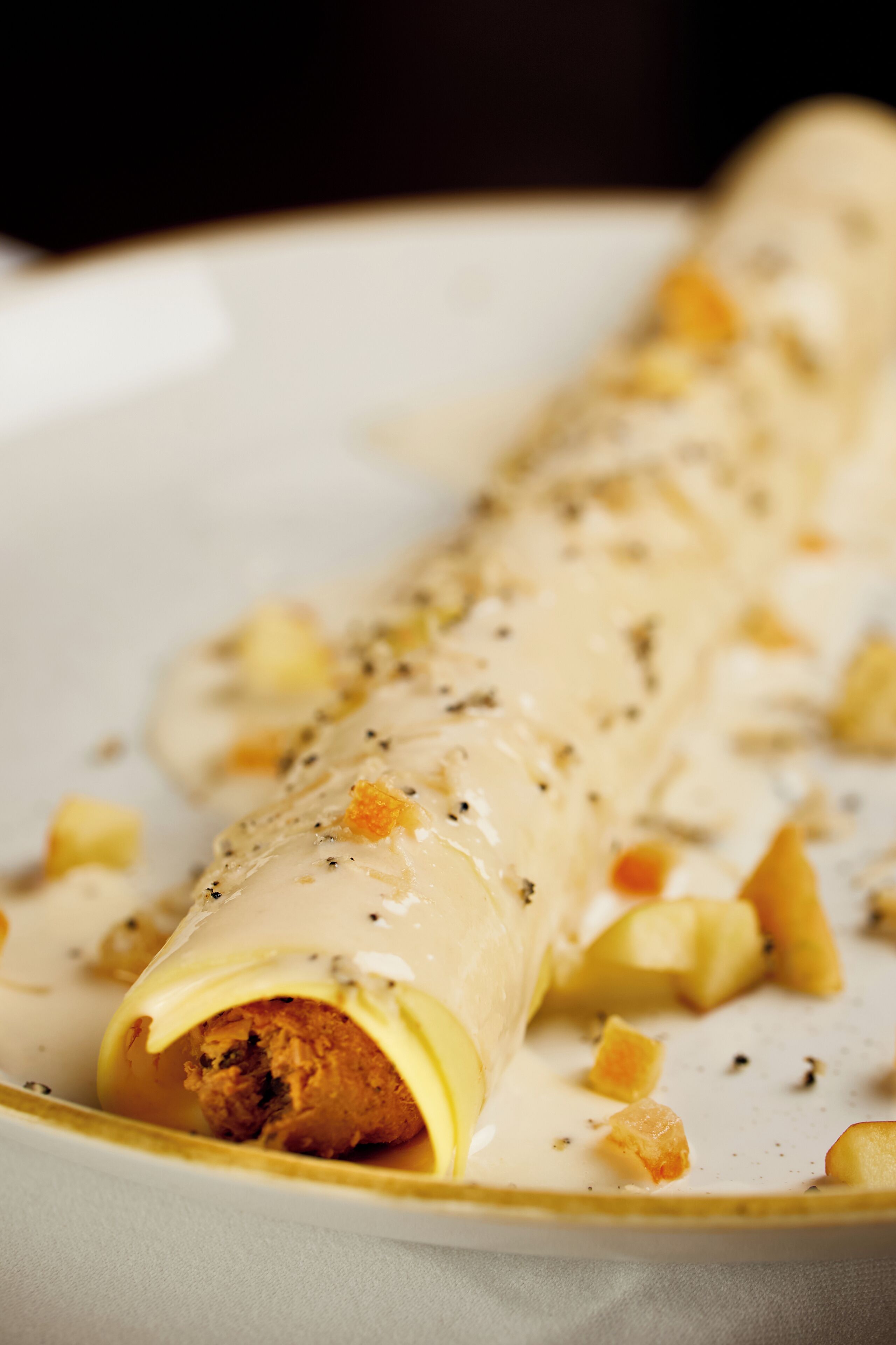 A rolled pastry with a creamy sauce and crumbled topping on a plate.