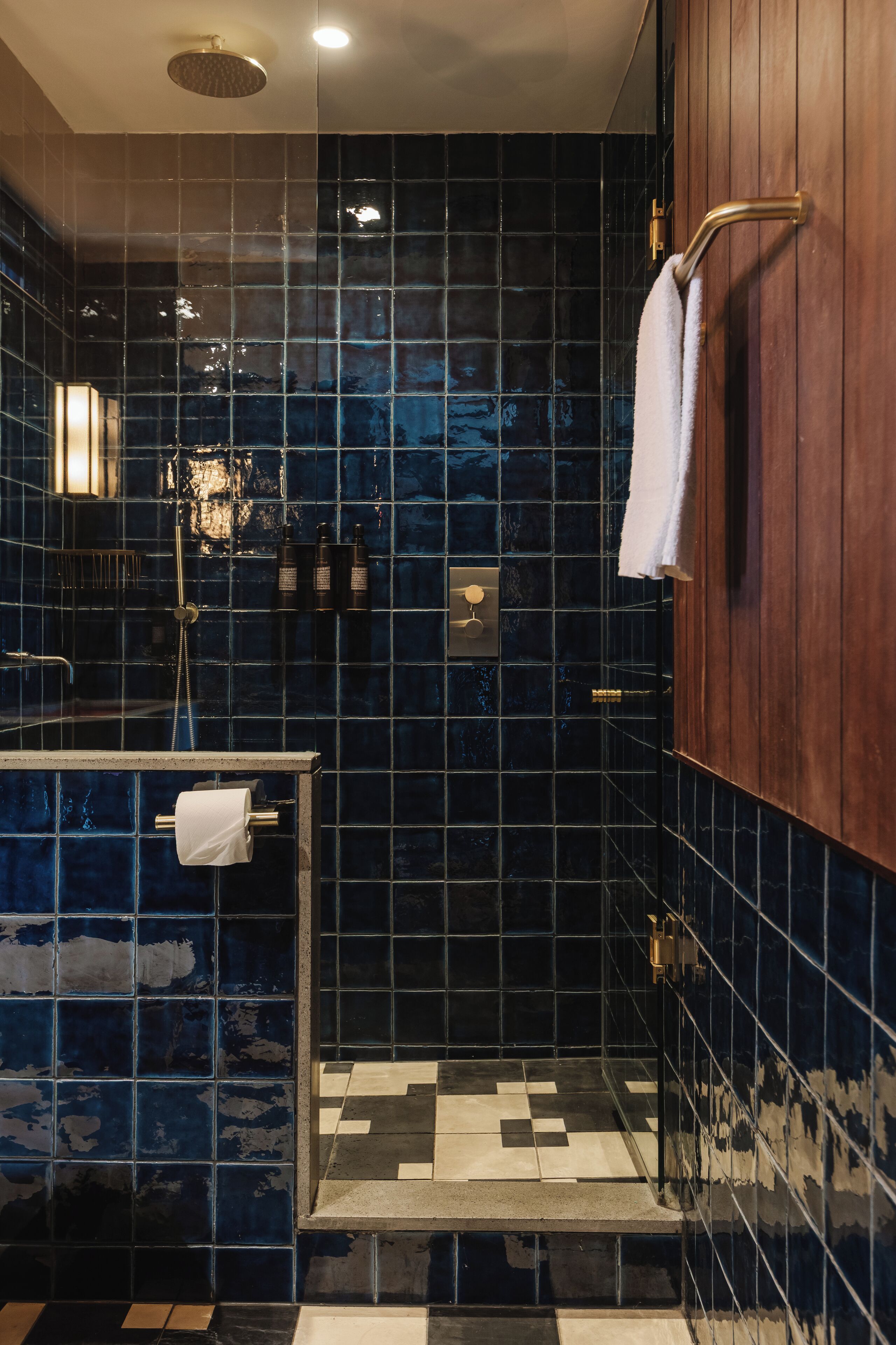 A bathroom with dark blue tiles, a wooden vanity, a towel rack, and a shower area.