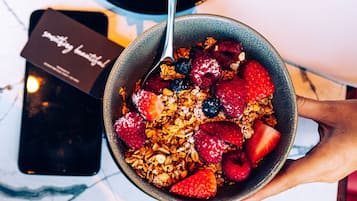 A bowl of granola with berries and a spoon, a smartphone, and a coffee cup on a table.