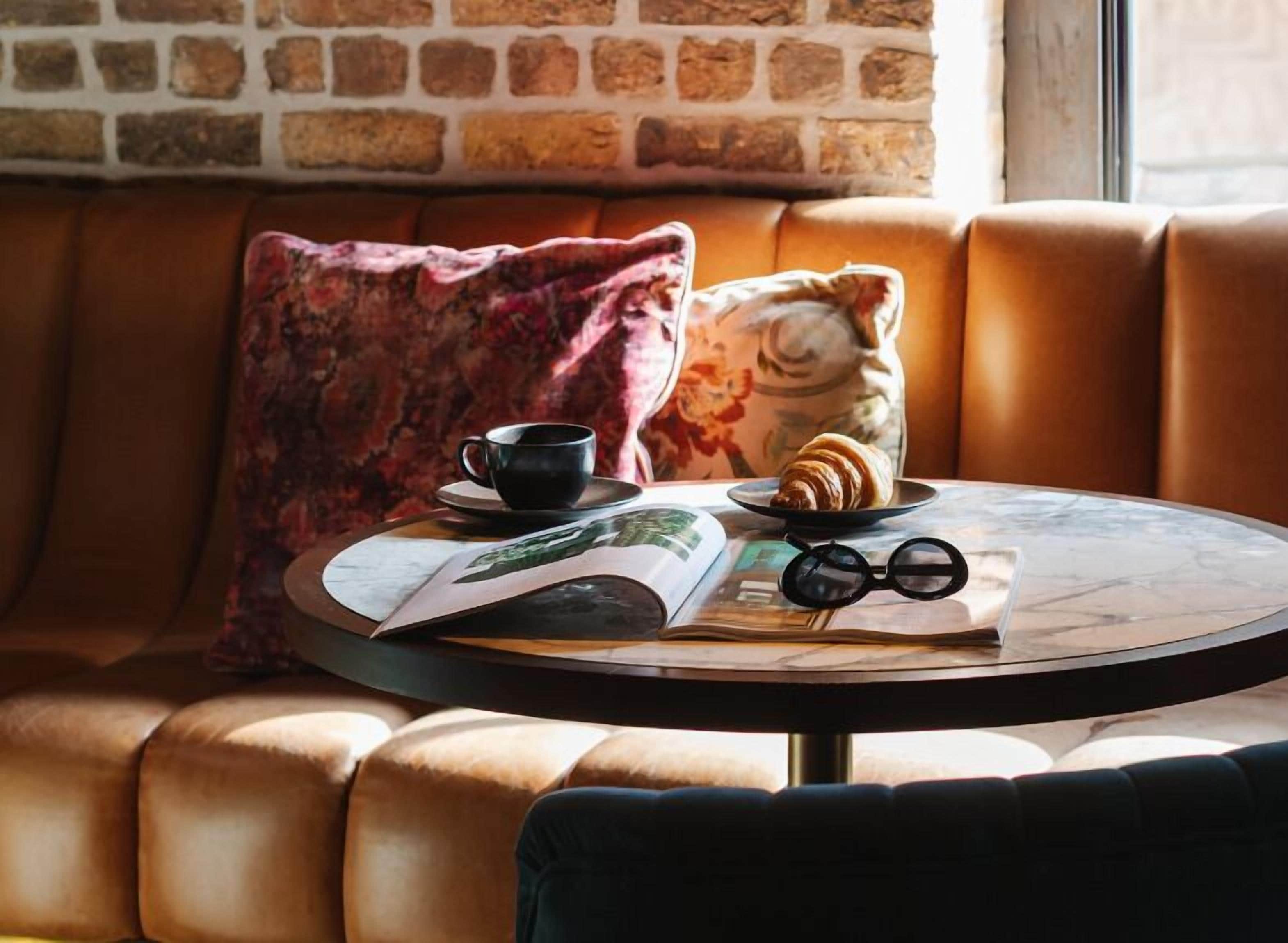 A round table with a book, a croissant, a cup, and a pair of glasses.