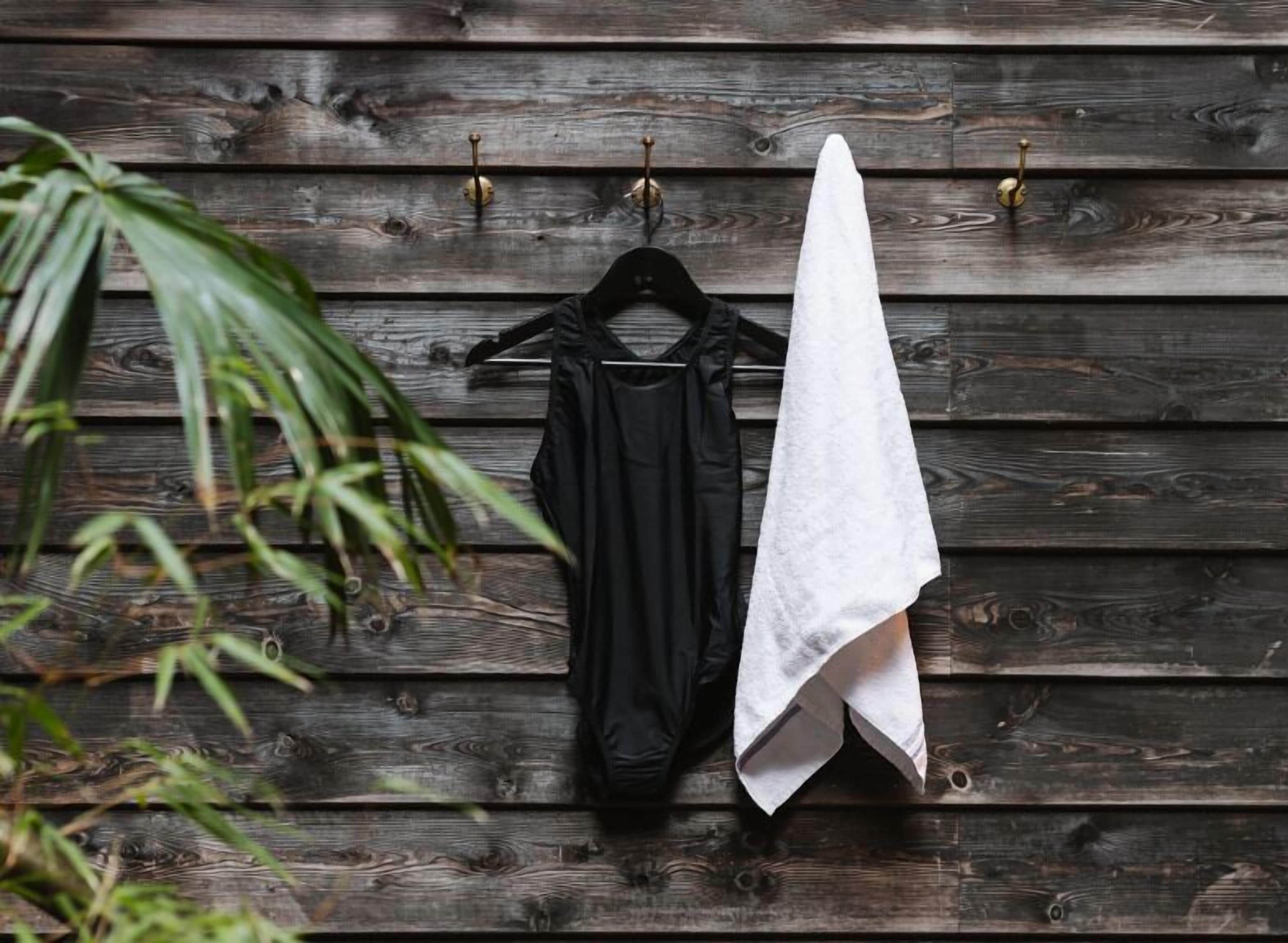 A wooden wall with a black garment and a white towel hanging on hooks.