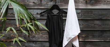 A wooden wall with a black garment and a white towel hanging on hooks.