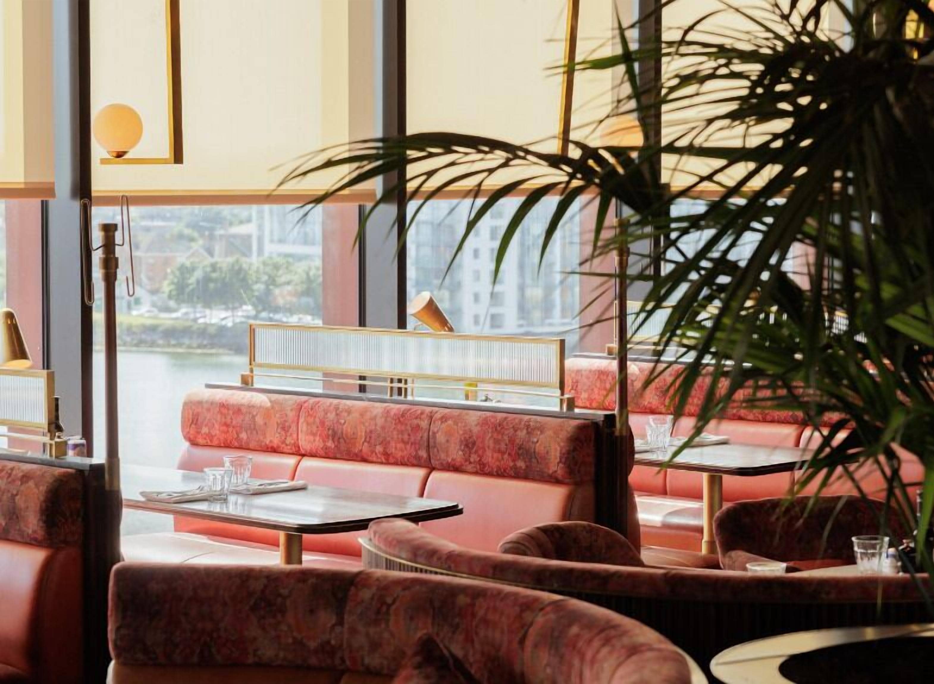 Een restaurant met rode bekleding, een piano en uitzicht op een rivier.