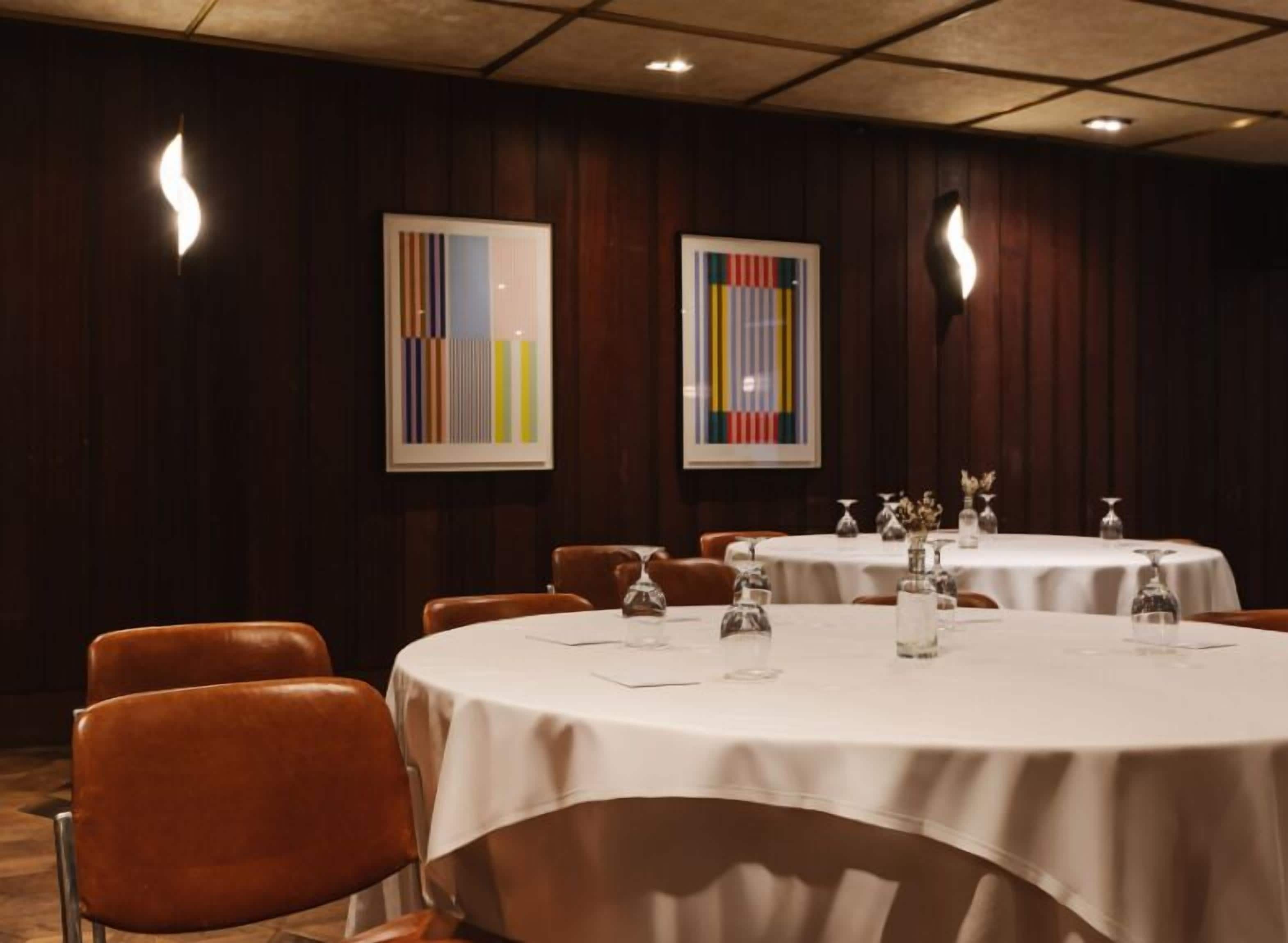A conference room with round tables, brown leather chairs, and framed abstract art on the walls.