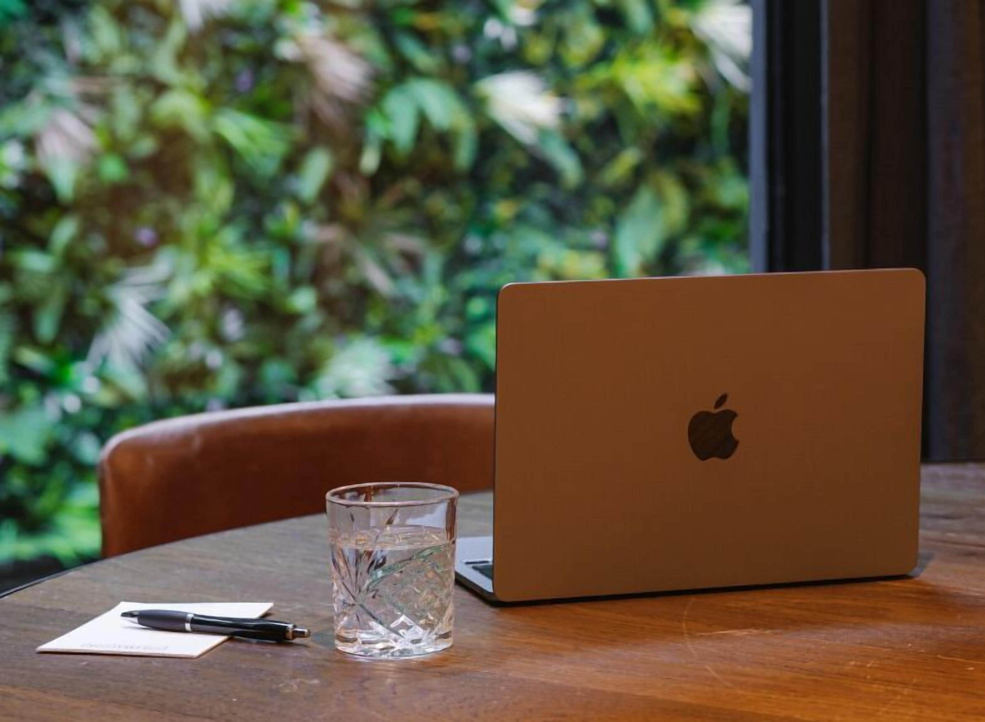 Un ordinateur portable est posé sur une table en bois, à côté se trouvent un verre d’eau et un stylo.