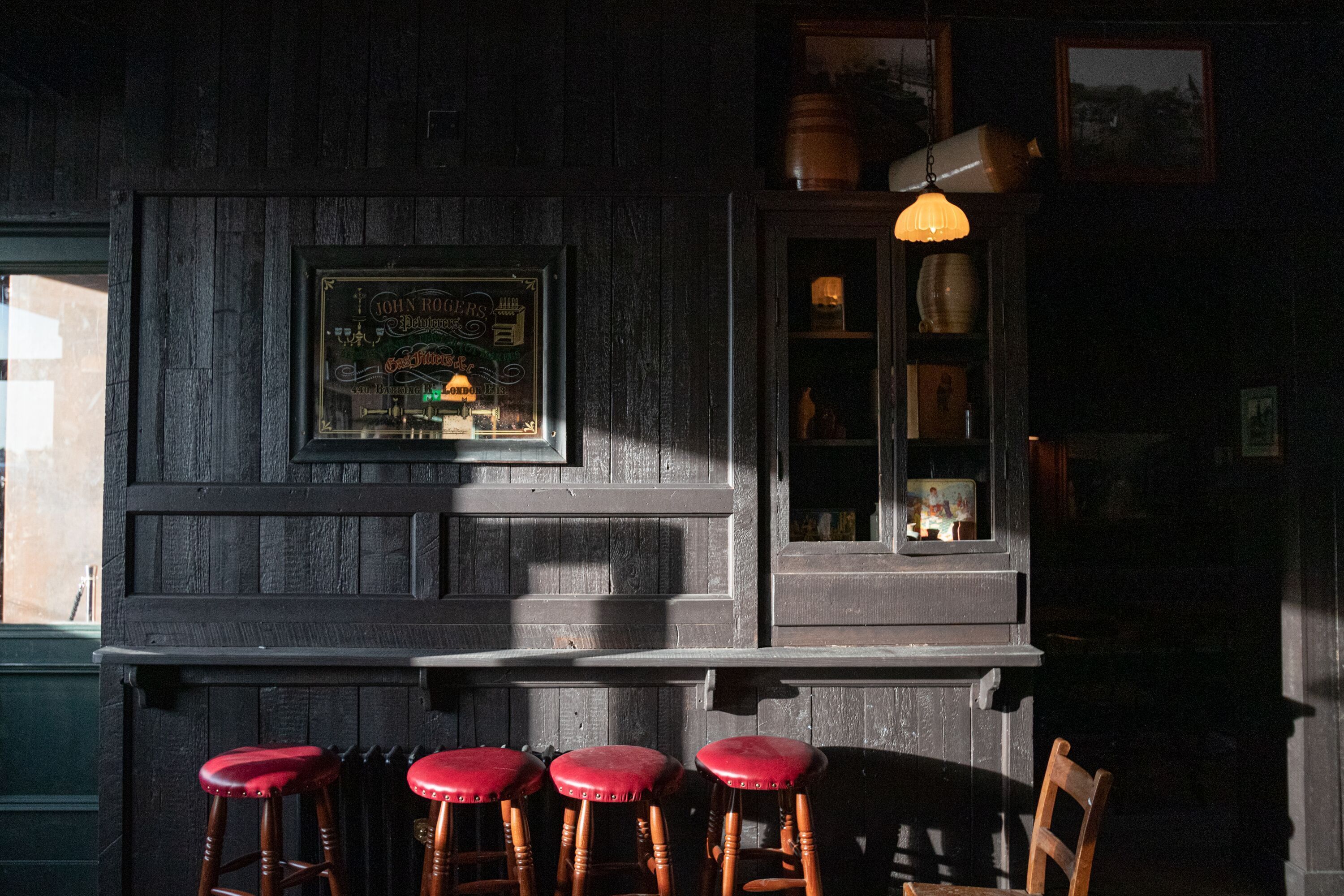 A bar area with wooden stools, a framed sign, and a hanging light fixture.