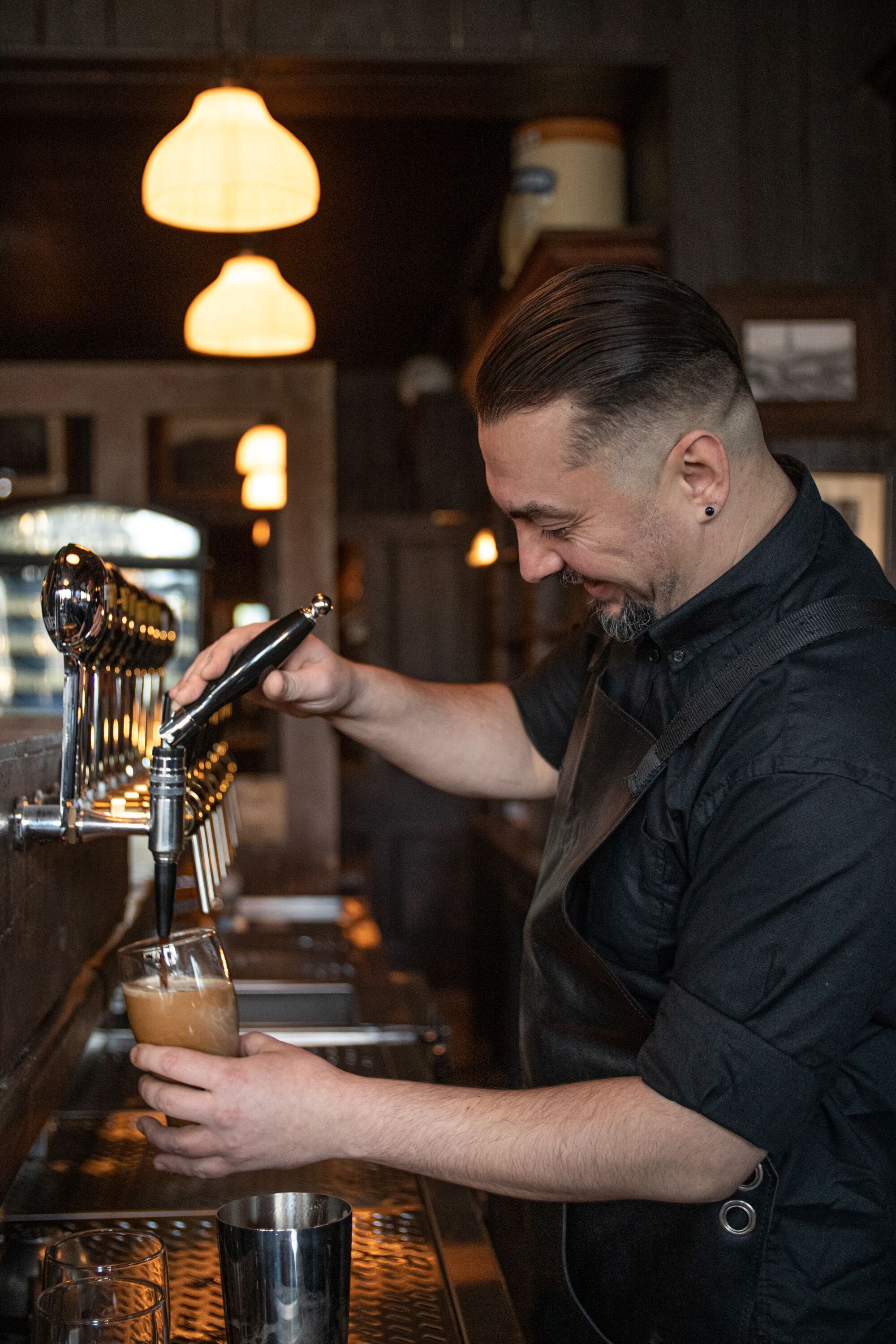 A bartender pouring a drink from a tap into a glass.