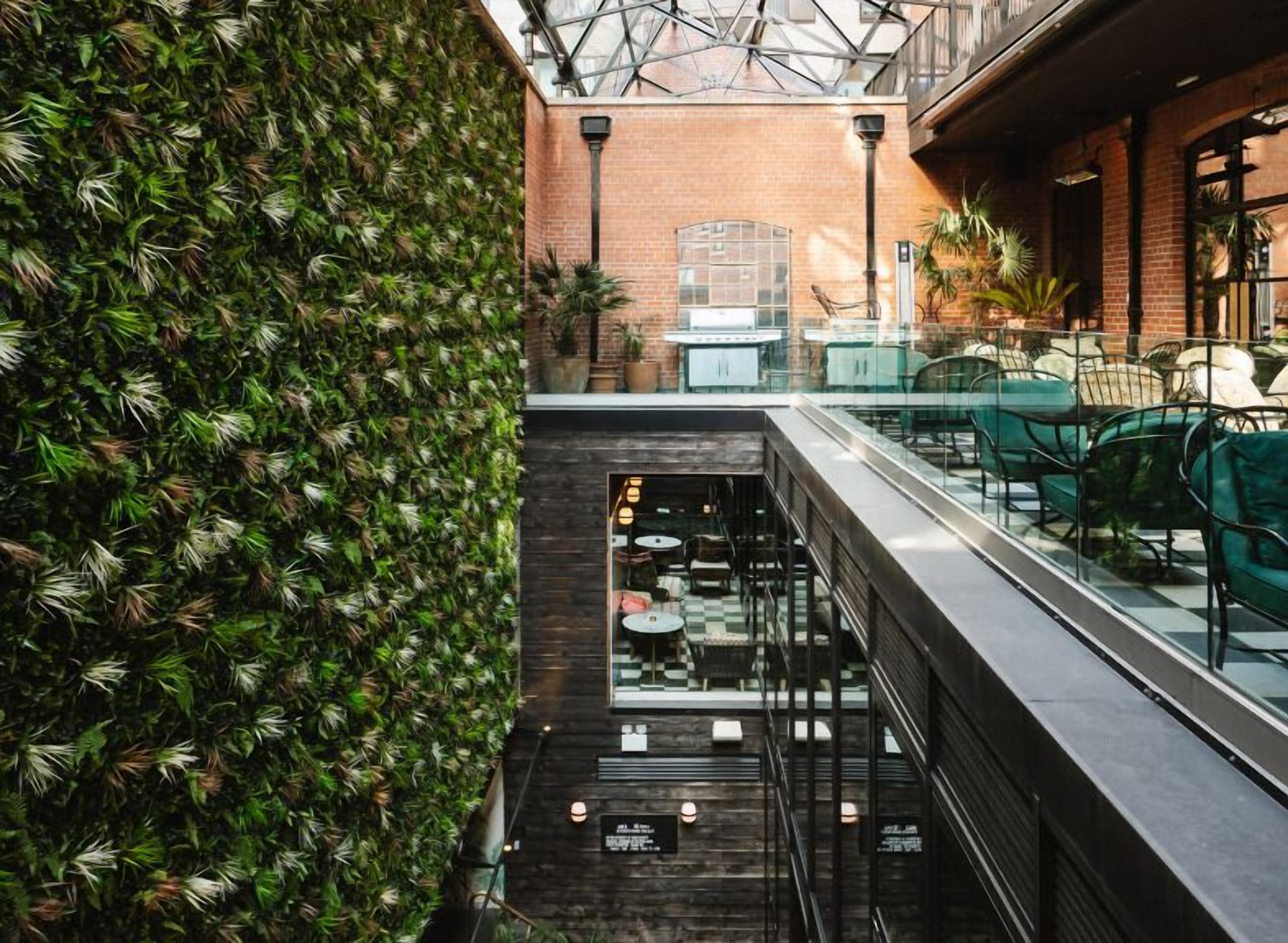 Un espacio interior moderno con techo de vidrio, asientos verdes y pared de ladrillo con plantas.