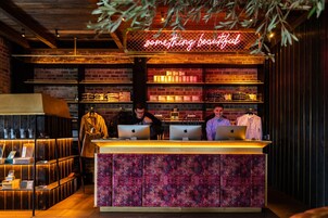 Zona bar con insegna al neon, mensole in legno e un bancone con tre persone.