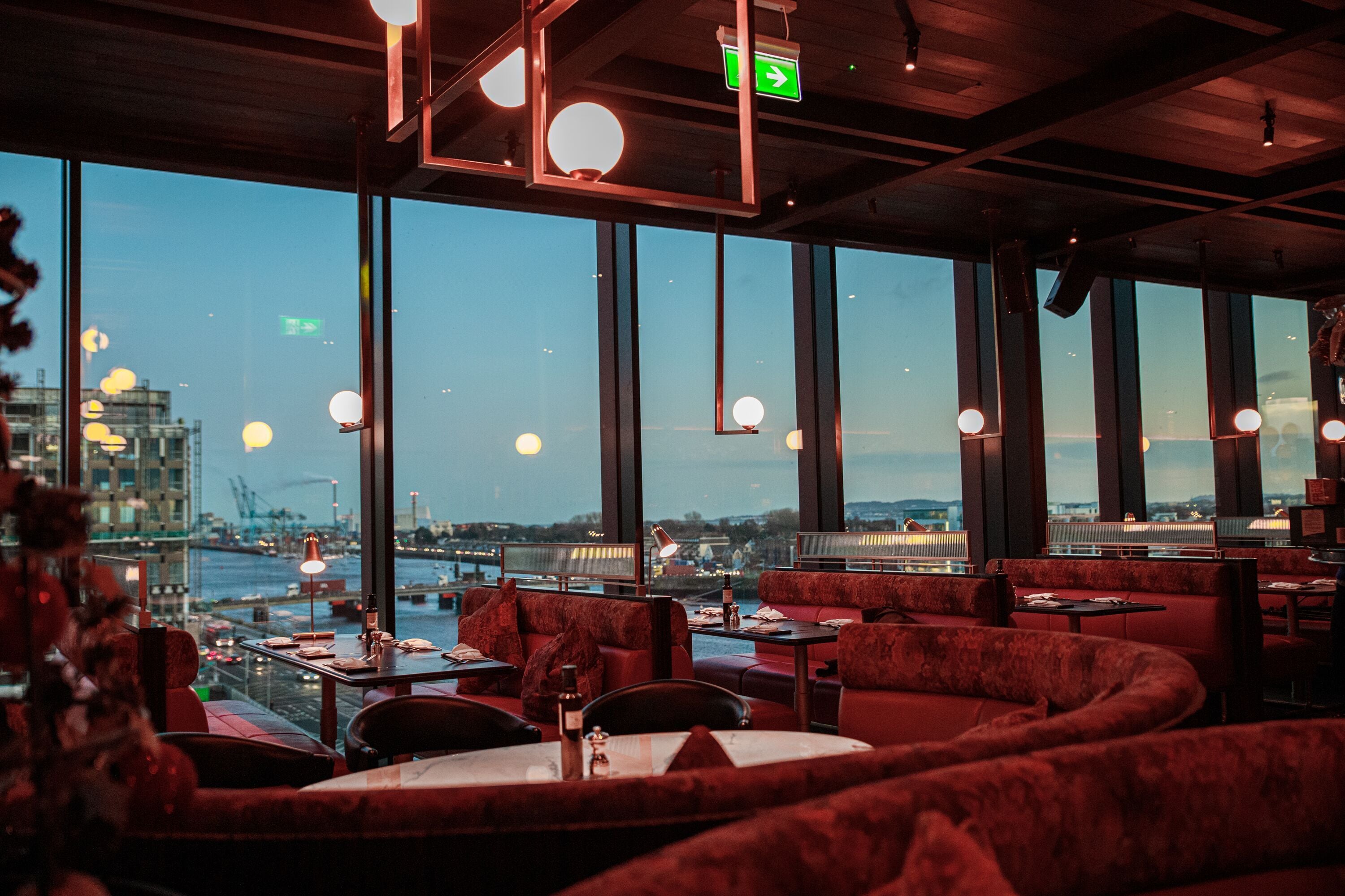 A restaurant with red upholstered seating, large windows, and a view of a cityscape.