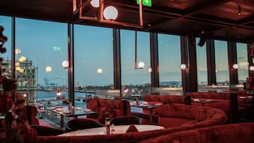 A restaurant with red upholstered seating, large windows, and a view of a cityscape.